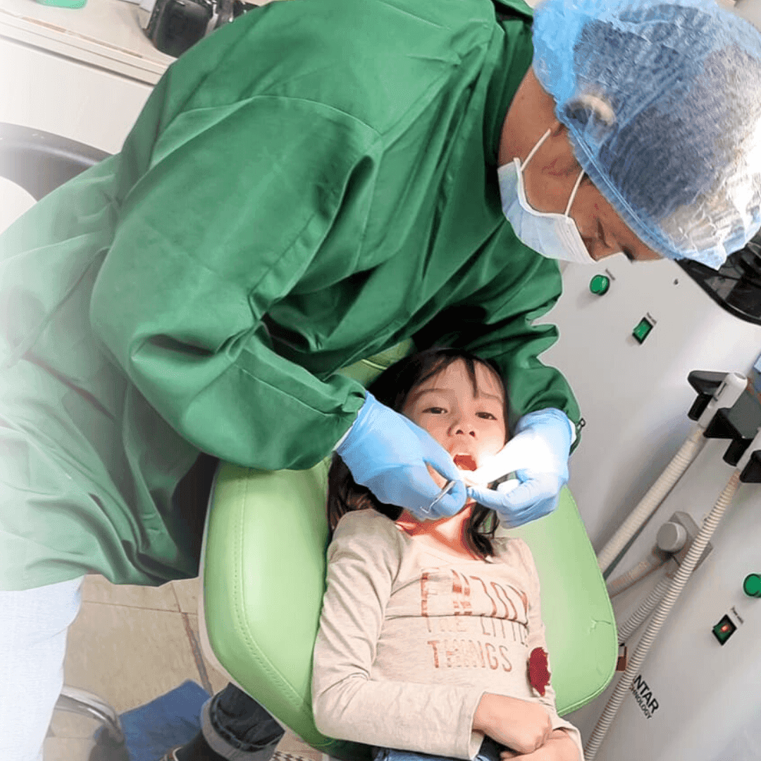 Dentist in green scrubs working on a young patient lying on a dental chair.