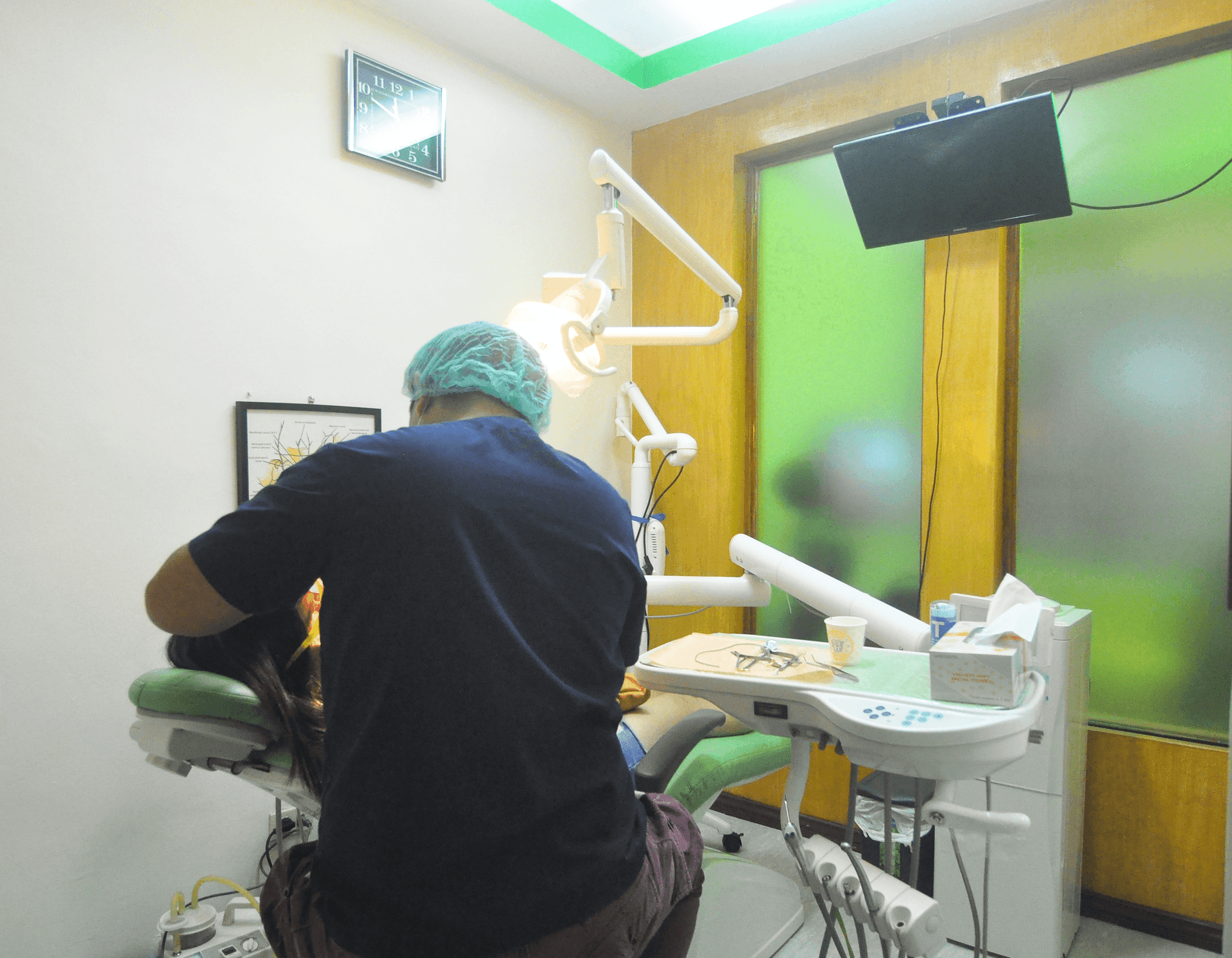 Dentist in blue scrubs treating a patient in a modern dental office with equipment and tools.